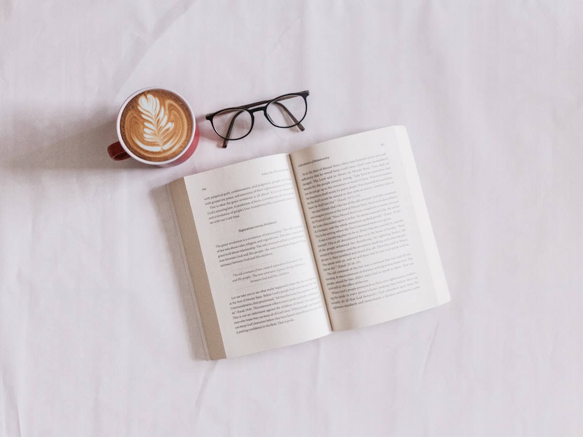 An open book, coffee and glasses on white linen